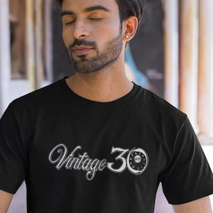 May include: A black t-shirt featuring a white graphic of the text "Vintage 30" and a vintage-style dial with numbers.