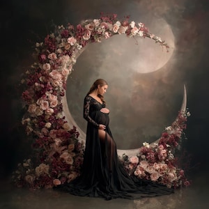 May include: A woman in a black maternity gown stands before a crescent moon backdrop adorned with flowers. The gown features long sleeves and a high slit. The flowers are a mix of pink and burgundy.