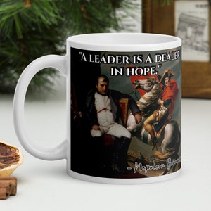 Może przedstawiać: Biały kubek ceramiczny z czarno-białym obrazkiem Napoleona Bonaparte na koniu. Kubek zawiera cytat Napoleona Bonaparte: "Lider jest handlarzem nadziei."