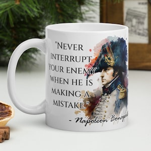 May include: White ceramic coffee mug with a watercolor illustration of Napoleon Bonaparte. The mug features a quote from Napoleon: "Never interrupt your enemy when he is making a mistake."