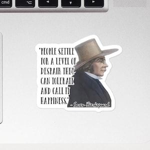 May include: A white sticker featuring a portrait of Søren Kierkegaard in profile, wearing a hat and glasses. The sticker includes the quote: "PEOPLE SETTLE FOR A LEVEL OF DESPAIR THEY CAN TOLERATE AND CALL IT HAPPINESS."
