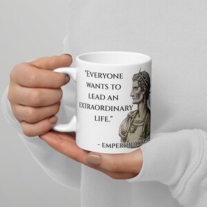 May include: White ceramic mug with a black and white illustration of a Roman emperor. The mug features the quote "Everyone wants to lead an extraordinary life." - Emperor Augustus.