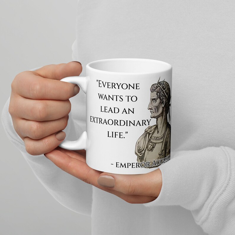 May include: White ceramic mug with a black and white illustration of a Roman emperor. The mug features the quote "Everyone wants to lead an extraordinary life." - Emperor Augustus.
