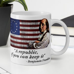 May include: White ceramic mug with a vintage American flag design and a portrait of Benjamin Franklin. The mug features the quote "A republic, if you can keep it" - Benjamin Franklin.