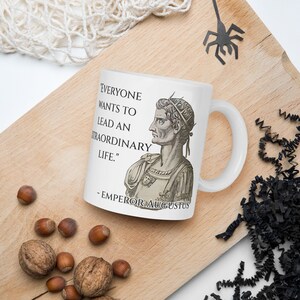 May include: White ceramic mug with a black and white image of a Roman emperor and a quote that reads "Everyone wants to lead an extraordinary life." - Emperor Augustus.