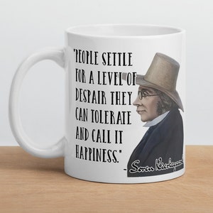 May include: White ceramic mug with a black quote that reads 'People settle for a level of despair they can tolerate and call it happiness.' The quote is attributed to Soren Kierkegaard. A drawing of a man with a hat and glasses is on the right side of the mug.
