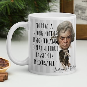 Puede incluir: Taza de cerámica blanca con una imagen en blanco y negro de Ludwig van Beethoven y una cita que dice: 'Tocar una nota equivocada es insignificante; tocar sin pasión es inexcusable.'