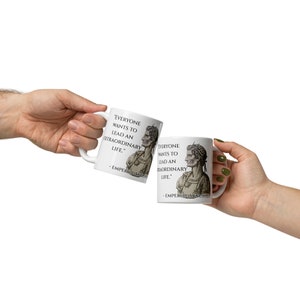 May include: Two white ceramic mugs with black text and a black and white image of a Roman emperor. The text on the mugs reads "Everyone wants to lead an extraordinary life." - Emperor Augustus.