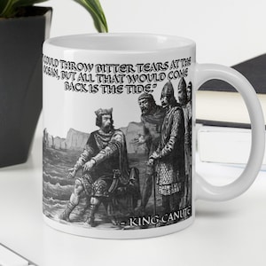 May include: White ceramic mug with a black and white illustration of King Canute, a historical figure, standing on a beach with his court. The quote "I could throw bitter tears at the ocean, but all that would come back is the tide" is printed on the mug.