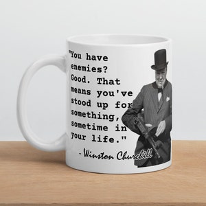 May include: White ceramic mug featuring a black and white image of Winston Churchill holding a gun. The mug displays a quote from Churchill: "You have enemies? Good. That means you've stood up for something, sometime in your life." -Winston Churchill