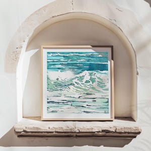 May include: A framed watercolor painting of ocean waves in shades of teal and blue. The artwork features a dynamic depiction of breaking waves with white foam and textured water. The painting is displayed in a light wood frame.