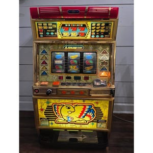 May include: A vintage slot machine with a gold-colored frame and a red top. The machine features the text "BIG CHANCE" and displays various fruit symbols. The bottom section has a yellow panel with a bird graphic and the text "A-type".