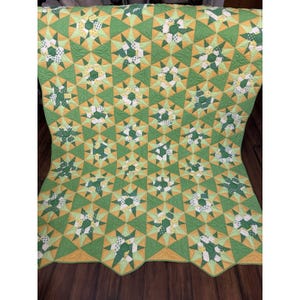May include: A handmade quilt featuring a repeating star pattern. The quilt showcases a vibrant color palette of green, yellow, and white. The star shapes are set against a green background, creating a visually appealing and cozy textile.