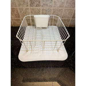 May include: A white wire dish rack with a built-in utensil holder. The rack has a rectangular shape with a grid design for holding plates and bowls. The base is a solid white tray to catch water.