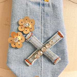 May include: A denim tie with embroidered flowers and gold sequin flowers. The tie has a denim X with rhinestones in the center.