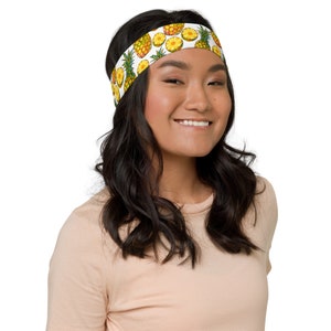 May include: A white headband with a pineapple pattern. The headband is being worn by a person with long, dark hair.