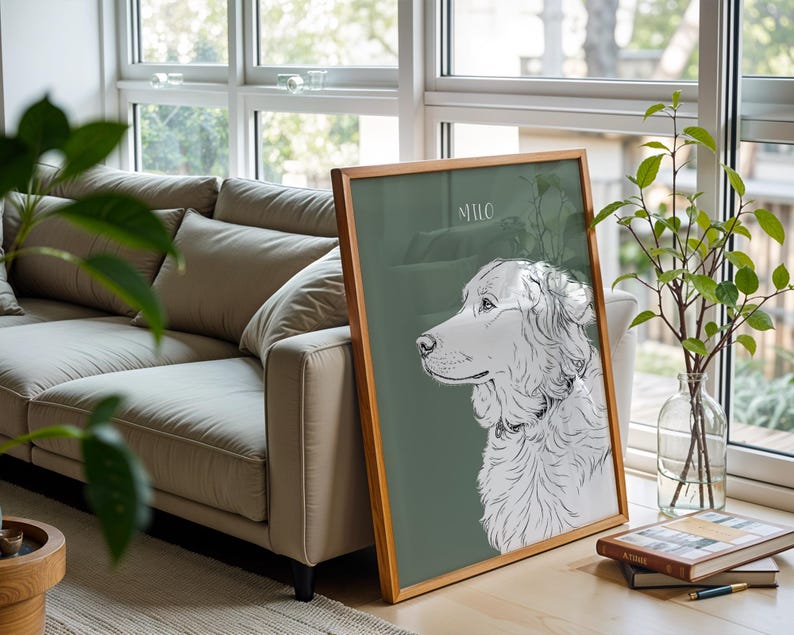 May include: A framed art print featuring a detailed black and white illustration of a dog's profile against a muted green background. The dog's name, "Milo," is written in a delicate font. The frame is made of light-colored wood.