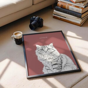 May include: A framed art print featuring a detailed illustration of a fluffy gray and white cat. The cat is set against a muted red background, with the name "LOWIE" printed at the top. The print is in a black frame.