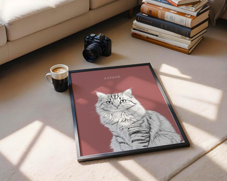 May include: A framed art print featuring a detailed illustration of a fluffy gray and white cat. The cat is set against a muted red background, with the name "LOWIE" printed at the top. The print is in a black frame.