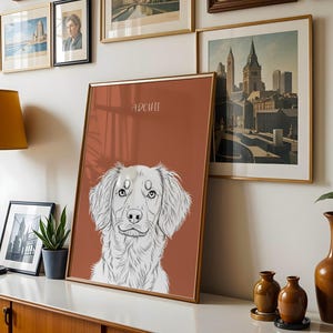 May include: A framed art print featuring a detailed black and white illustration of a dog's face, with the name "Archie" above. The print has a rust-colored background and a gold frame. Other framed art and decor are visible.
