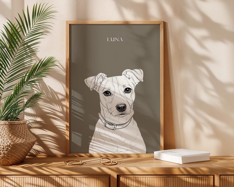 May include: A framed art print featuring a detailed sketch of a dog's face, set against a muted gray background. The dog is white with black accents, wearing a collar. The name "LUNA" is printed at the top. The frame is made of wood.