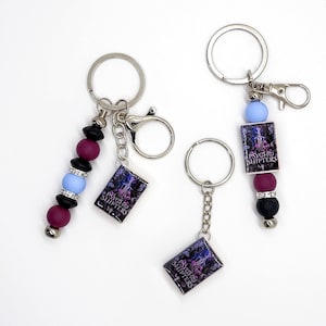 May include: Keychains with the text "Psycho Shifters" on small rectangular charms. The keychains have silver rings and chains, with decorative beads in black, blue, and purple. One keychain has a clasp.