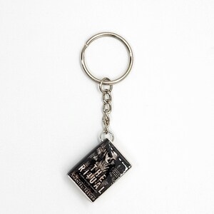 May include: A silver keychain with a rectangular charm featuring the book cover of "The Ritual" by Shantel Tessier. The charm has a black and white design with the book title and author's name visible.