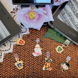 May include: A set of nine Harry Potter themed book marks. The book marks are made of metal and feature different characters and symbols from the Harry Potter series. The book marks are displayed on a brown wicker surface.