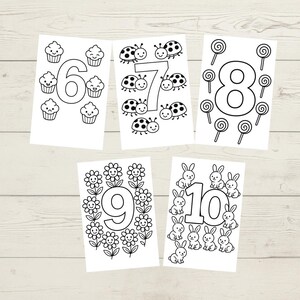 May include: Five white cards with black outlines of numbers 6 through 10. Each number is decorated with a different theme: cupcakes, ladybugs, lollipops, flowers, and bunnies. The cards are arranged on a light wood-grain surface.