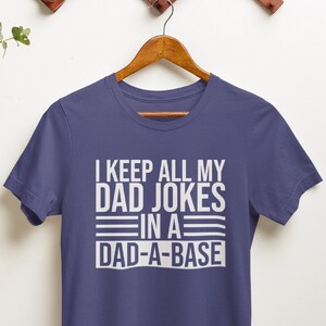 May include: A purple t-shirt with white text that reads "I keep all my dad jokes in a dad-a-base".