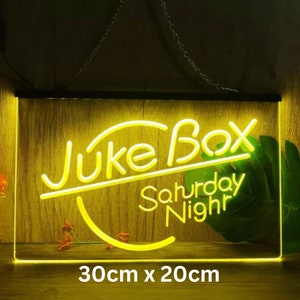 May include: Yellow neon sign with the text "Jukebox Saturday Night" on a wooden background. The sign is 30 inches by 20 inches.