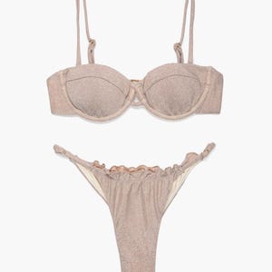 Puede incluir: Un conjunto de bikini de dos piezas en un color champán brillante. La parte superior es un bikini estructurado con aros y tirantes ajustables. La braguita es de corte alto con volantes.