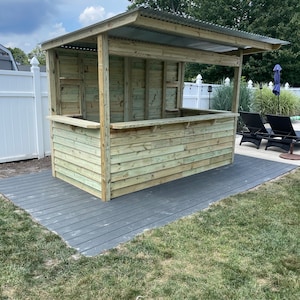 May include: A wooden outdoor bar with a corrugated metal roof, a gray composite deck, and green grass.
