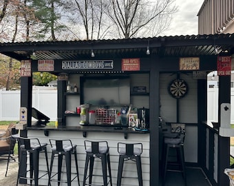 May include: An outdoor bar area with a black and white bar, four black metal bar stools, and a dartboard. The bar has a sign that says "Dallas Cowboys Ave".