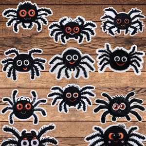 May include: A set of 14 black embroidered spider patches with white outlines and orange eyes. The spiders have different facial expressions and are arranged on a wood background.