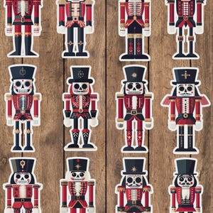 May include: A collection of twelve decorative stickers featuring stylized nutcracker figures with a Day of the Dead theme. Each nutcracker is dressed in a red and black uniform with a top hat and skull face. The stickers are arranged on a wooden background.