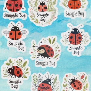 May include: A collection of stickers featuring cartoon ladybugs with the text "Snuggle Bug". The ladybugs are red with black spots and black heads. Some stickers have floral accents, set against a watercolor blue background.