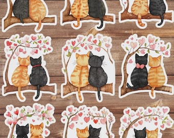 May include: A collection of stickers featuring watercolor illustrations of two cats perched on a tree branch. The cats are in various colors, including black, orange, and calico, with pink heart-shaped leaves and flowers.