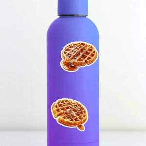 May include: A purple water bottle adorned with two waffle stickers. The waffles are golden brown with syrup. The bottle has a matching purple cap and a smooth finish. The stickers are placed on the front of the bottle.