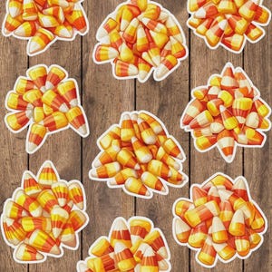 May include: Nine stickers featuring candy corn, a classic Halloween treat. Each sticker shows a cluster of the tri-colored candies with white, yellow, and orange segments. The stickers are set against a wooden background.