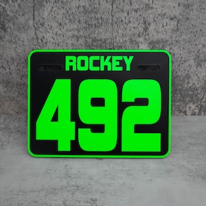 May include: Black and green plastic race number plate with the text "ROCKEY" and the number "492" in large green font.