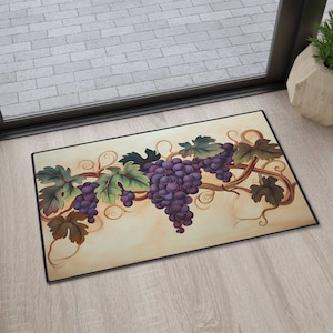 May include: A decorative doormat with a beige background featuring a painted design of purple grapes hanging from a vine with green leaves.