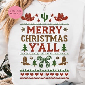 May include: White sweatshirt with a festive design featuring cowboy hats, a cactus, boots, and a bow. The text "MERRY CHRISTMAS Y'ALL" is displayed in a rustic font, perfect for the holiday season.