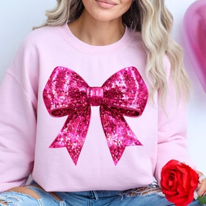 May include: A pink sweatshirt with a large sparkly pink bow design on the front.