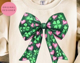 May include: A cream-colored sweatshirt with a green and pink bow design. The bow is made up of shamrocks and hearts.