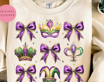 May include: A cream-colored sweatshirt with a festive Mardi Gras design. The design features purple, gold, and green bows, a crown, a fleur-de-lis, a jester's hat, and a mask.