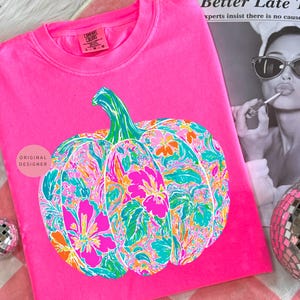 May include: A bright pink Comfort Colors sweatshirt featuring a colorful floral pumpkin design. The pumpkin has a green stem and is filled with pink, orange, and teal floral patterns. The words "ORIGINAL DESIGNER" are printed on the shirt.