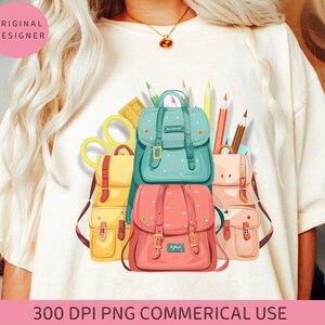 May include: A white t-shirt with a graphic of colorful backpacks and school supplies. The backpacks are in various colors and styles, including blue, yellow, pink, and green. The school supplies include pencils, scissors, and a ruler.