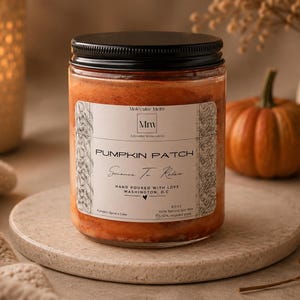 May include: A glass jar candle with a black lid, filled with orange wax. The label reads "Pumpkin Patch" and "Science To Relax". A small pumpkin and decorative items are in the background. The candle is on a round, stone-like surface.