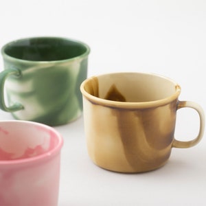May include: Three ceramic mugs with a marbled glaze. The mugs are in shades of green, yellow, and pink.